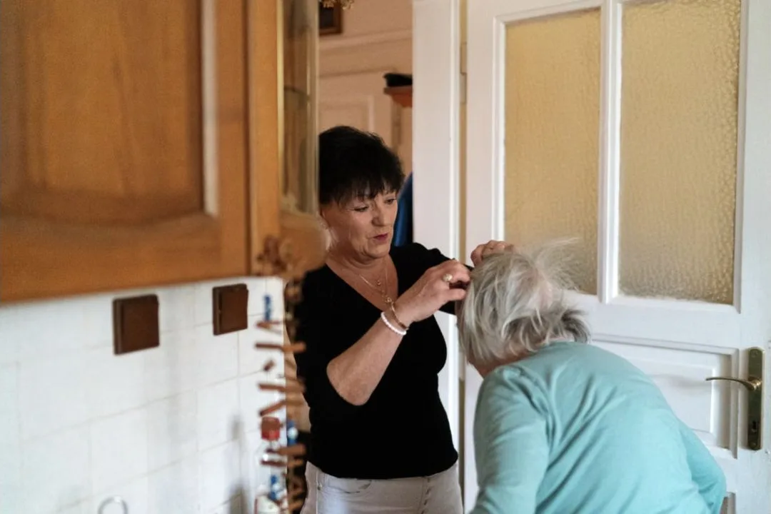 Caregiver helping an older woman with hair grooming at home